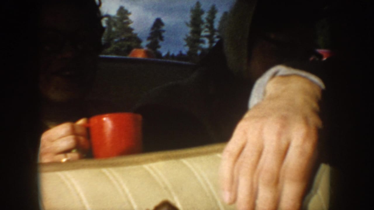 Person in dark winter clothing holds a red mug beside a pale car seat.