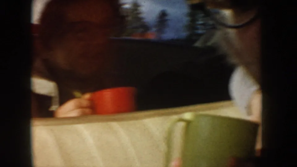 1955 Idaho home-movie frame of car passengers, one with a red mug, filmed close to pale upholstery and a window view.
