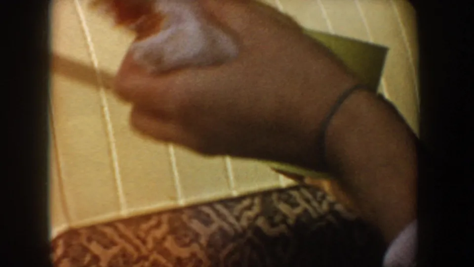 1955 Idaho road-trip frame showing a hand holding a small snack above pale car upholstery, with patterned fabric below.
