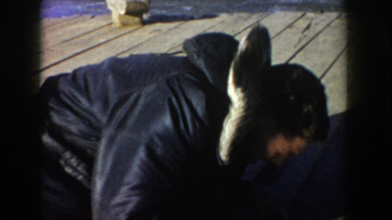 Adult man in a dark hooded jacket bends over a wooden dock surface.