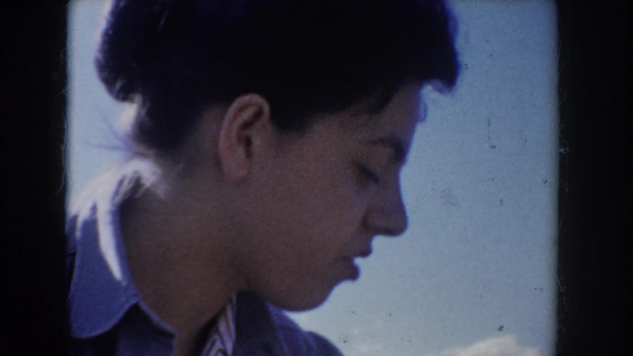 Tight close-up profile of a young woman with short dark hair wearing a light blue jacket, looking downward against a bright blue sky, Idaho USA, circa 1955.