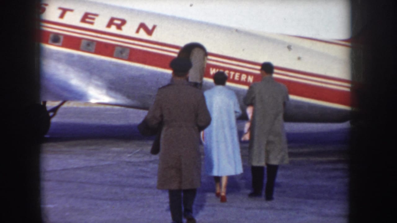 8mm frame showing three figures in 1950s dress — including a person in a light blue coat — walking toward a Western Airlines aircraft on the tarmac, c.1955.