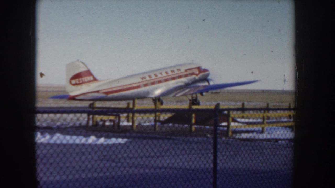 Western Airlines propeller aircraft moving along airfield, chain-link fence in foreground, snow on ground.