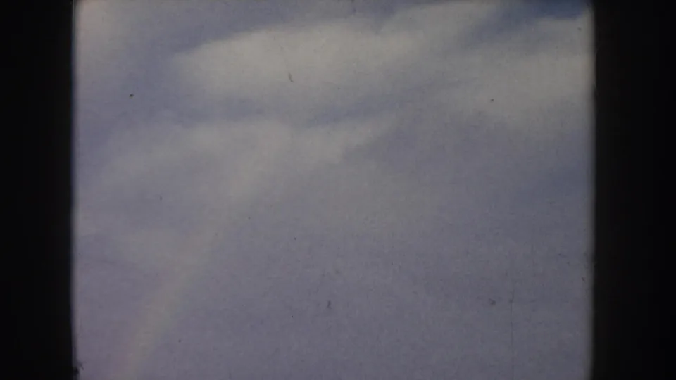 8mm home movie, Idaho c.1955 — dramatic cumulus clouds billow against a blue sky filling the entire frame, film grain and dust specks visible throughout.