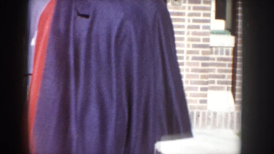 Accidental close-up of a man's dark suit jacket; brick building wall visible at right, red vehicle at left edge; Idaho street, circa 1955 per metadata.