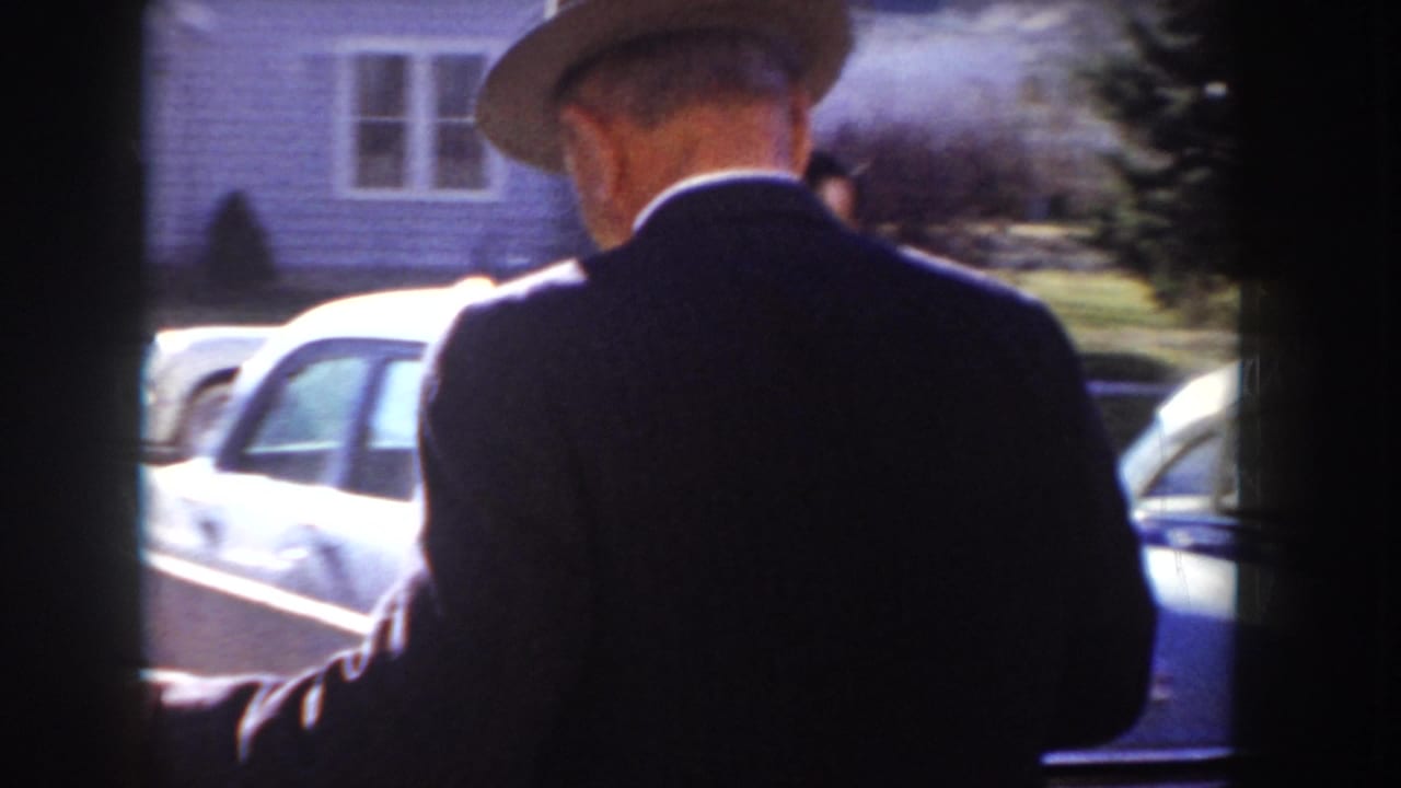 Rear view of a suited man in wide-brimmed hat walking toward classic 1950s cars on a suburban street, Idaho, USA, circa 1955.