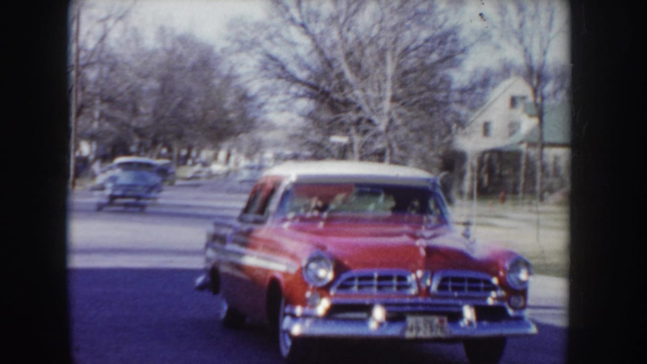 Mid-1950s red and white two-tone sedan driving toward camera on a residential street in Idaho, USA, circa 1955; a second period car visible behind.