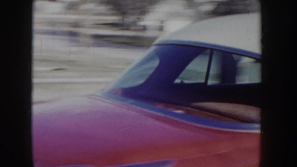 Passing side view of a red mid-1950s American sedan showing the curved roofline and side window, captured on color 8mm film circa 1955.