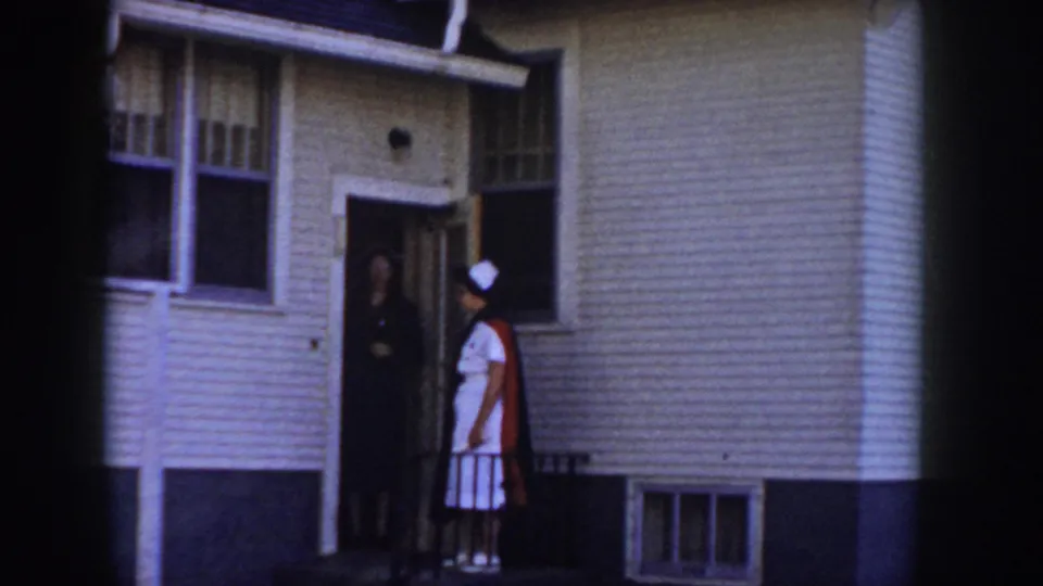 Nurse at the doorway of a low ranch-style suburban home, greeted by a figure in the doorway, Idaho USA circa 1955.