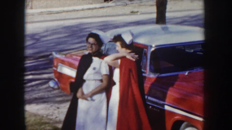 Two women pose beside a red and white two-tone sedan in what appears to be Idaho, circa 1955; one wears a white nurse uniform and cap.