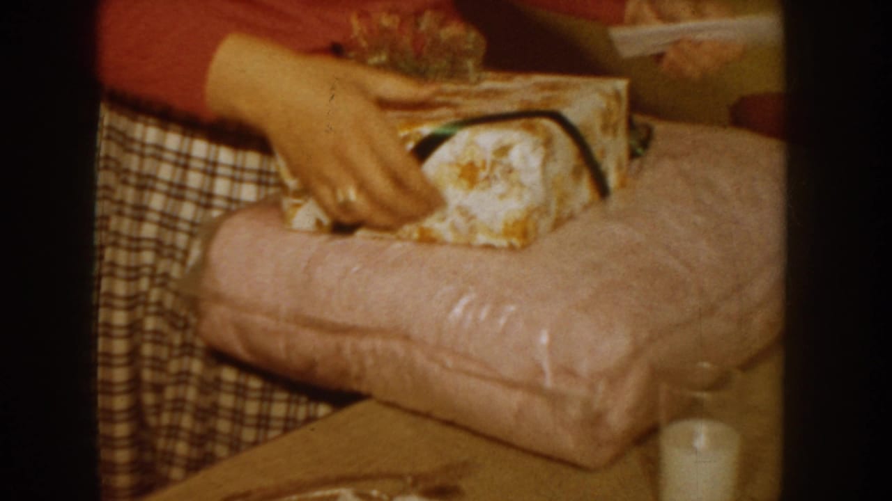 Close-up of hands handling a floral-wrapped gift box with a dark ribbon resting on a pink surface.