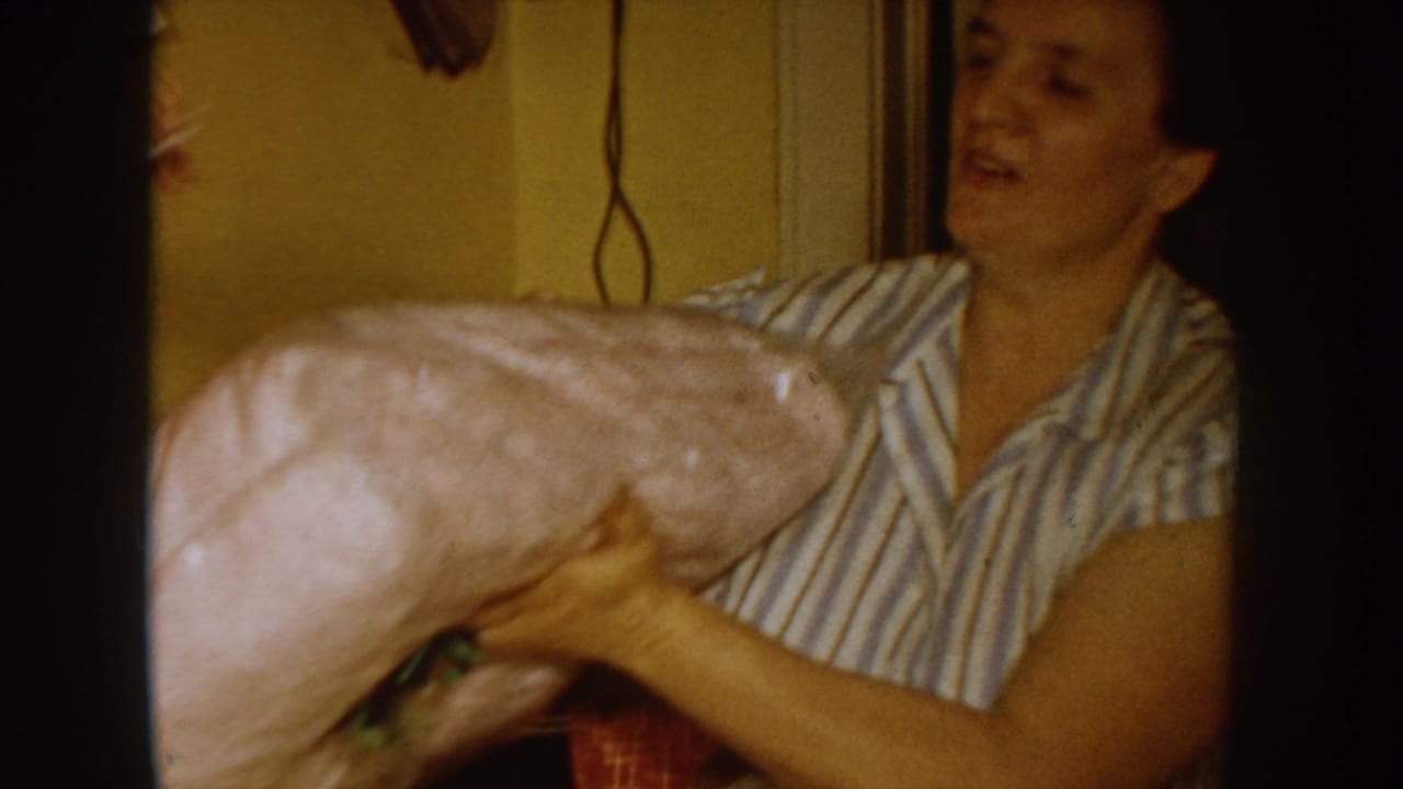 Woman in a mid-1950s striped sleeveless blouse unwraps a large pink-paper parcel in what appears to be a home kitchen, Idaho USA, circa 1955