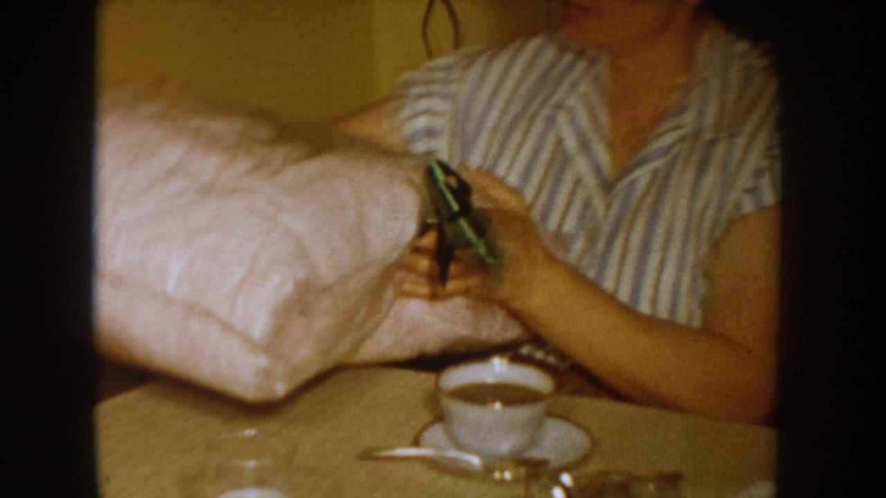 Woman's hands on a large pink-wrapped parcel beside a white coffee cup and saucer on a surface