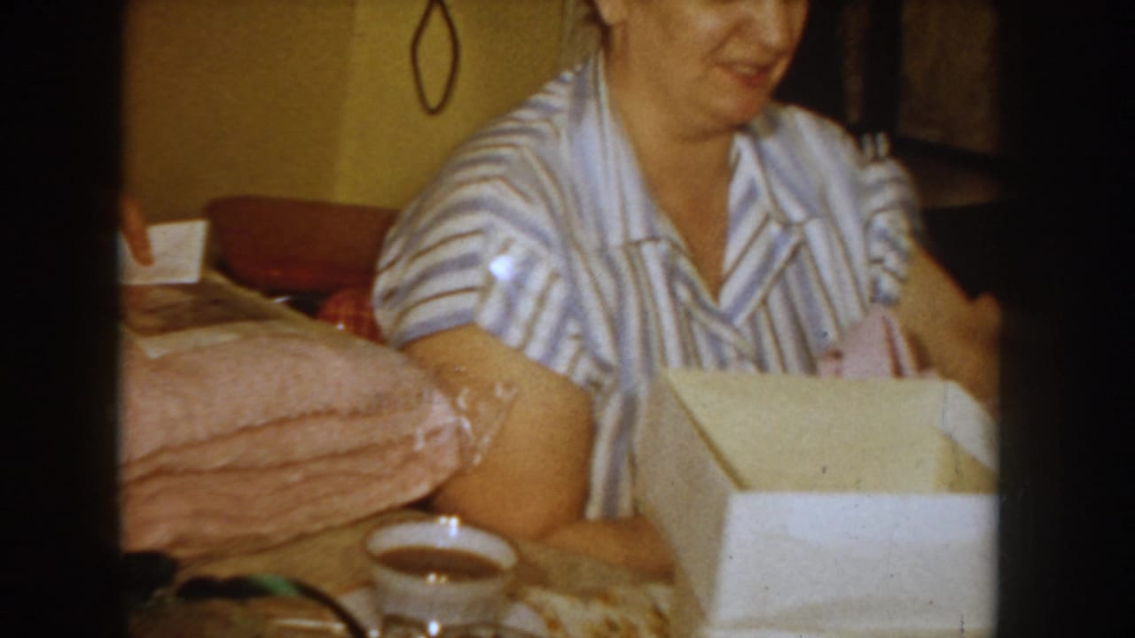Woman in blue-and-white striped dress holding a pink garment lifted from an open white gift box, smiling.