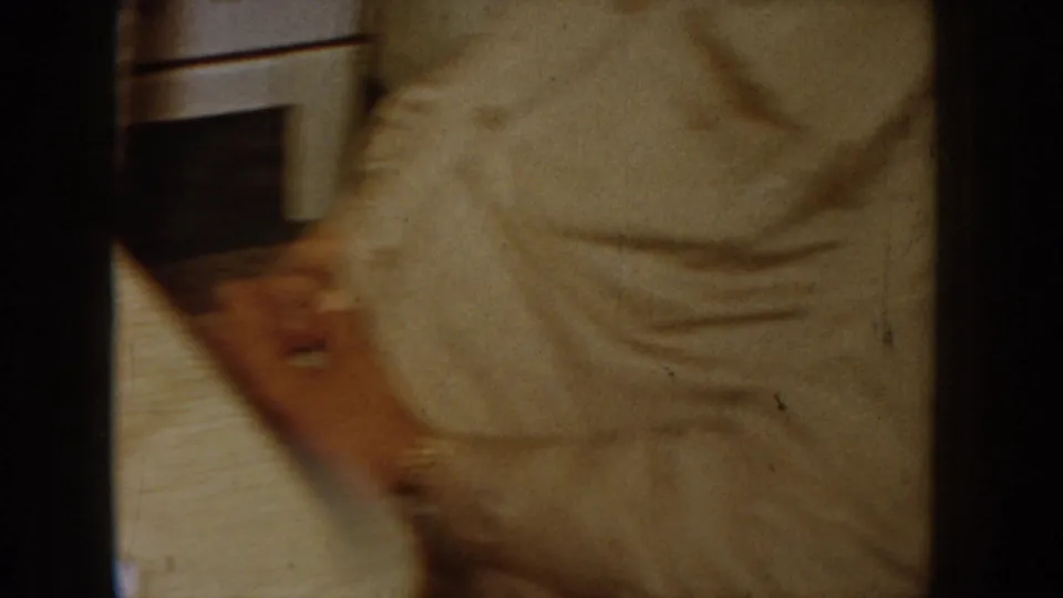 Camera pan produces heavy motion blur across light-colored clothing with a table surface below, Idaho home movie circa 1955.