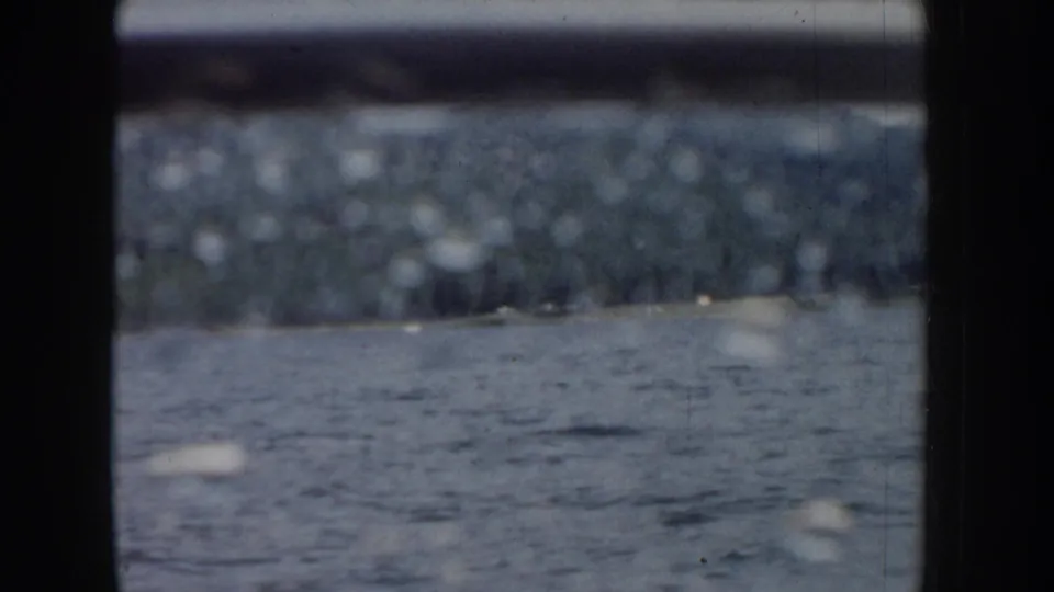 8mm home movie frame from a moving boat on an Idaho lake, circa 1955; dark window borders frame a view of rippled water and a distant blurred treeline.