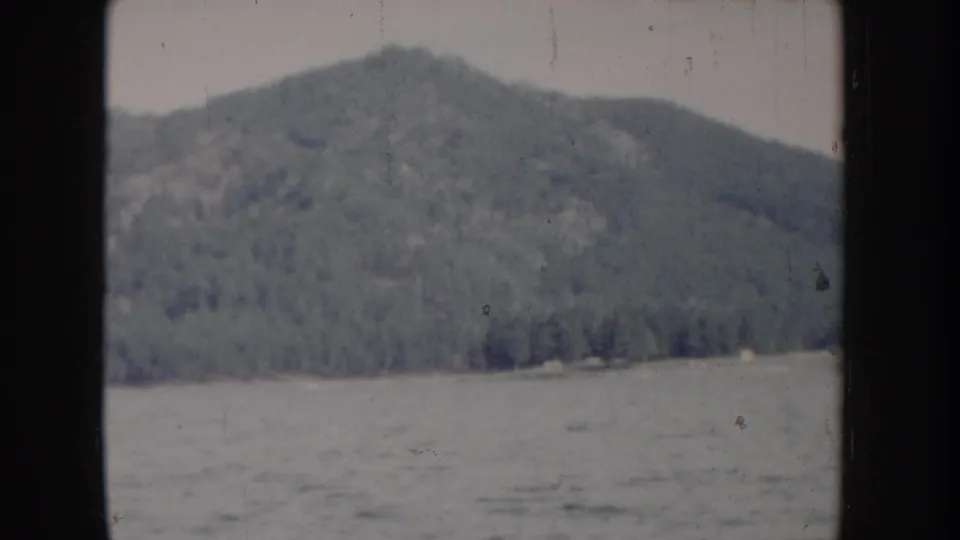 8mm home movie circa 1955, Idaho — panned view of rounded conifer-covered mountain above choppy lake surface from boat.