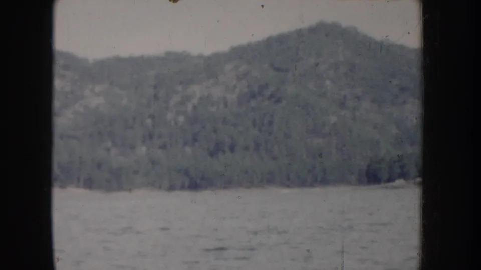 8mm home movie circa 1955, Idaho — continued boat-POV pan of conifer-covered mountain above open lake water.