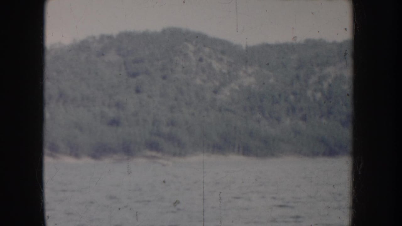 Nearly identical 8mm frame of calm lake and forested hillside, consistent fading and grain throughout.