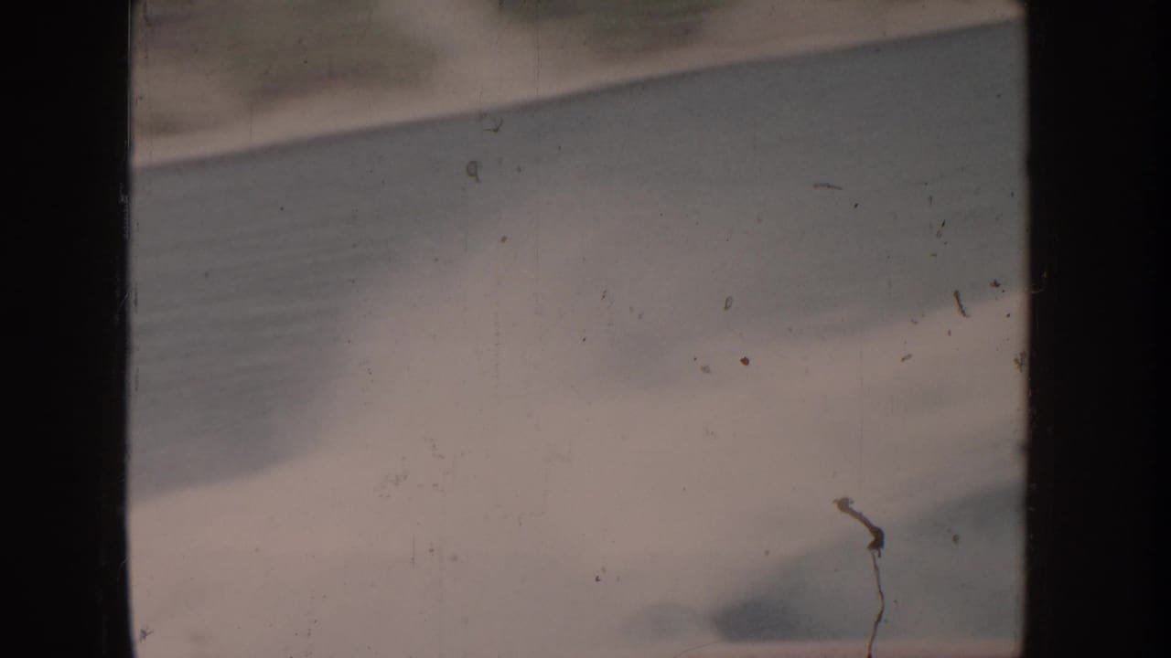 Heavily bleached 8mm film frame; faint wave shapes at lower edge; thin dark vertical element at right may be a flagpole but is not clearly identifiable