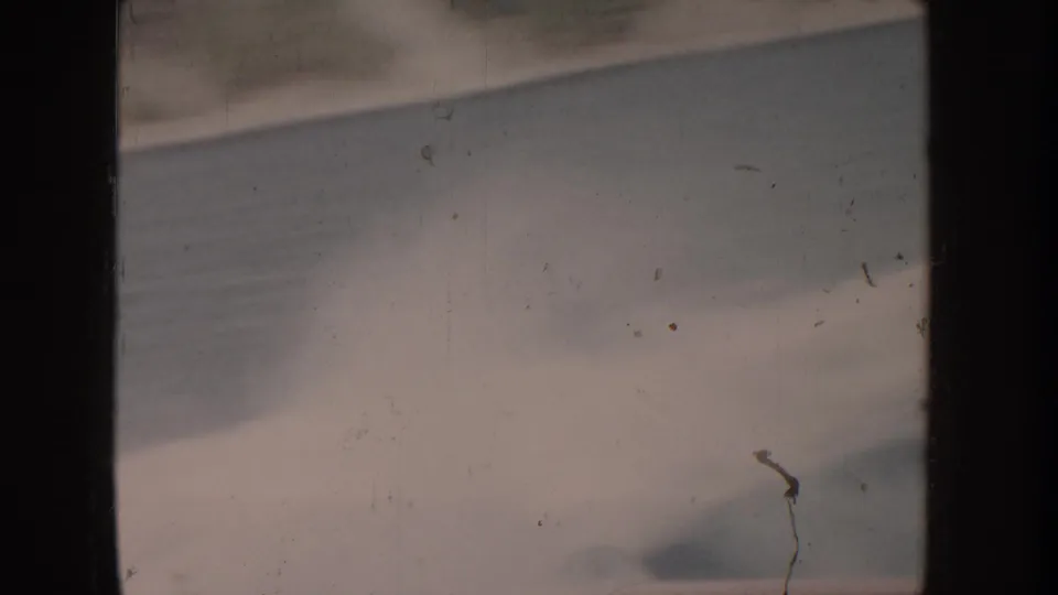 Heavily bleached 8mm film frame; faint wave shapes at lower edge; thin dark vertical element at right may be a flagpole but is not clearly identifiable