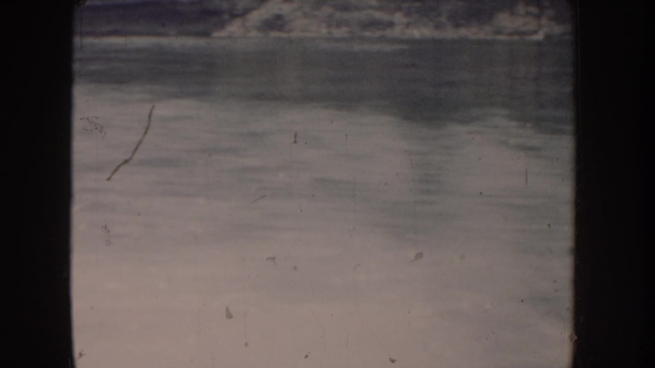 Lake surface filmed from a moving boat in 1955 Idaho; pale pink-beige color fading typical of aged 8mm film, with distant shore visible at top of frame.