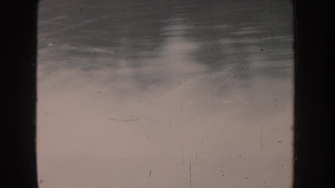 Heavily overexposed 8mm frame; faint distant shape on water, nearly all detail lost to color fading.