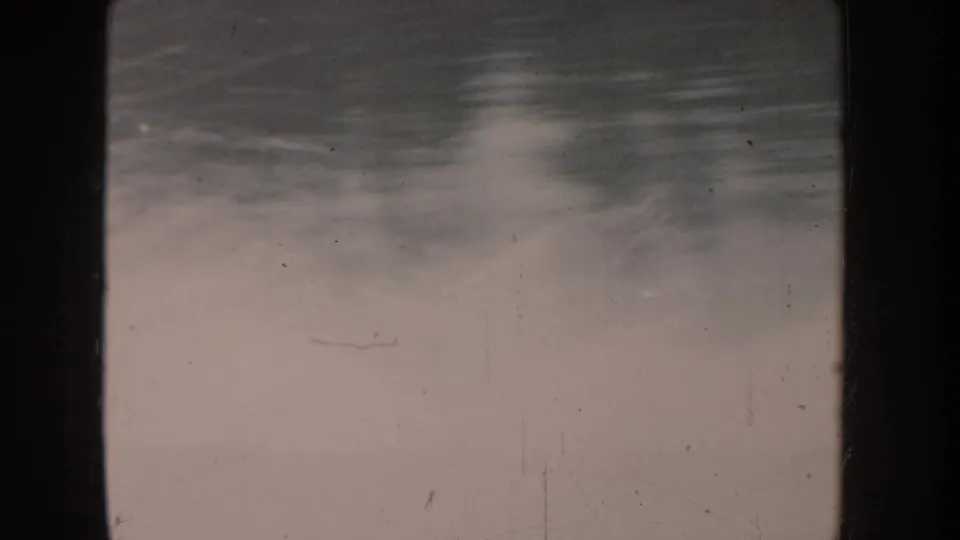 Severely faded 8mm frame with minimal recoverable detail; a faint elongated shape, possibly a small boat, is barely discernible on the water surface.
