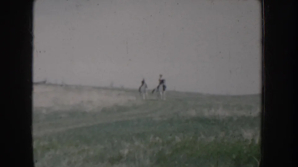 Two riders on horseback silhouetted on the ridgeline of an open grassy hillside, shot on 8mm film in rural Idaho, circa 1955.