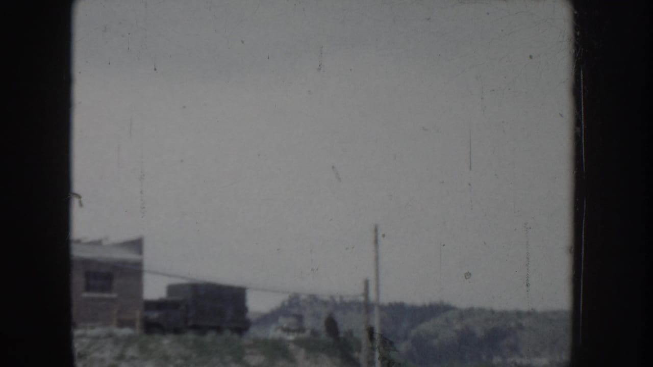 Overexposed 8mm film frame from what may be Idaho, circa 1955, showing a distant building, hills, and utility poles.