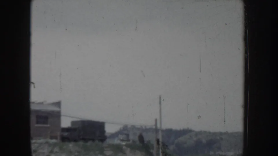 Overexposed 8mm film frame from what may be Idaho, circa 1955, showing a distant building, hills, and utility poles.