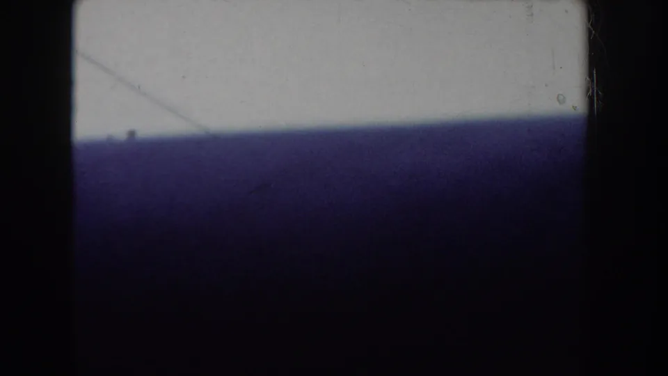 Dark 8mm frame, possibly filmed past a purple curtain or fabric close to the lens, with a glimpse of an exterior scene below.