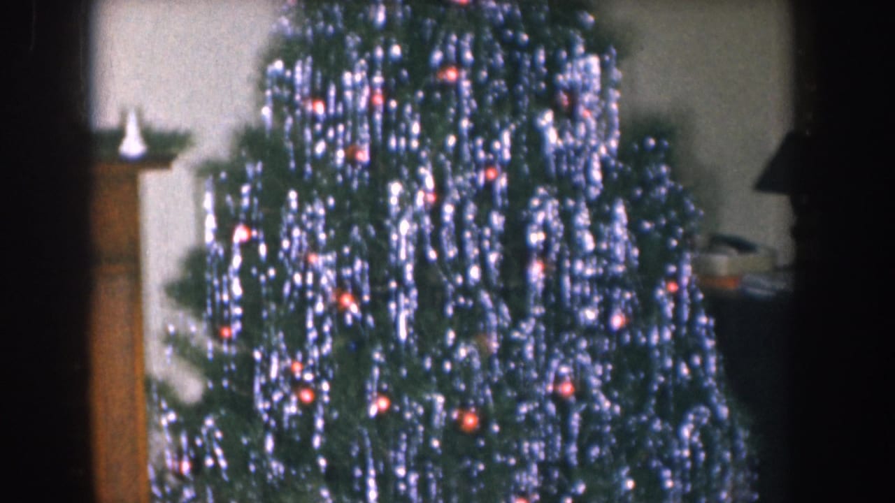 Tinsel-draped Christmas tree at left; wooden fireplace mantel with white decorations and framed painting partially visible at right.