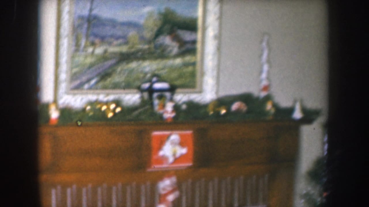 Fireplace mantel with garland and figurines; framed rural landscape oil painting more fully visible above; camera slightly panned right.