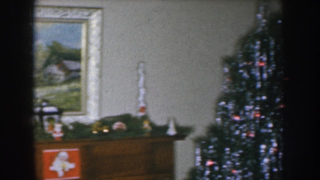 1950s American living room showing framed landscape painting on wall, wooden sideboard with holiday figurines, and Christmas tree with silver tinsel — Nebraska, circa 1955