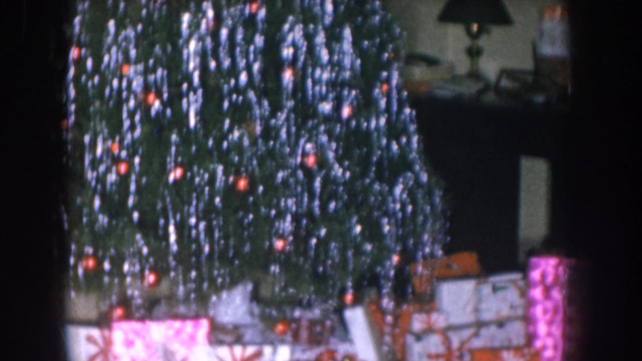 Close-up of Christmas tree with dense silver icicle tinsel and orange bulb lights, wrapped gifts in pink and orange below