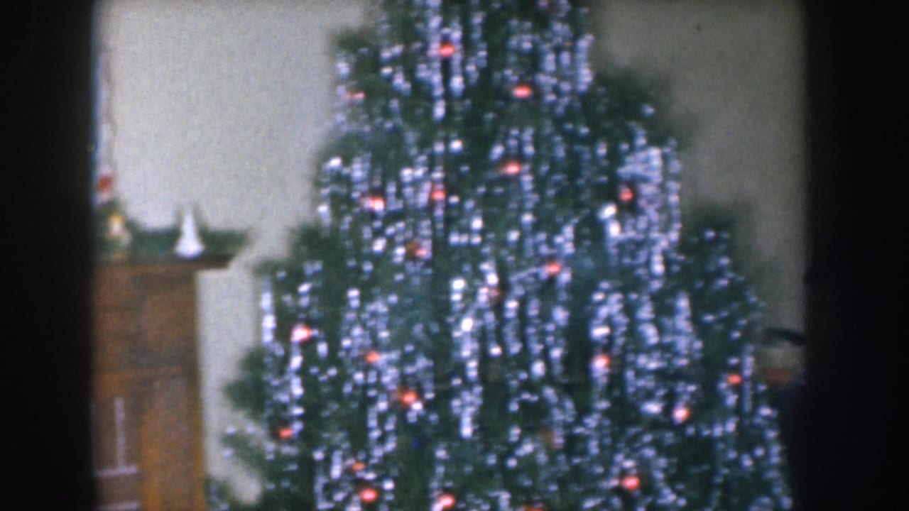 Tinsel-laden Christmas tree with red lights and a fireplace mantel visible at left, from a Nebraska home movie circa 1955.