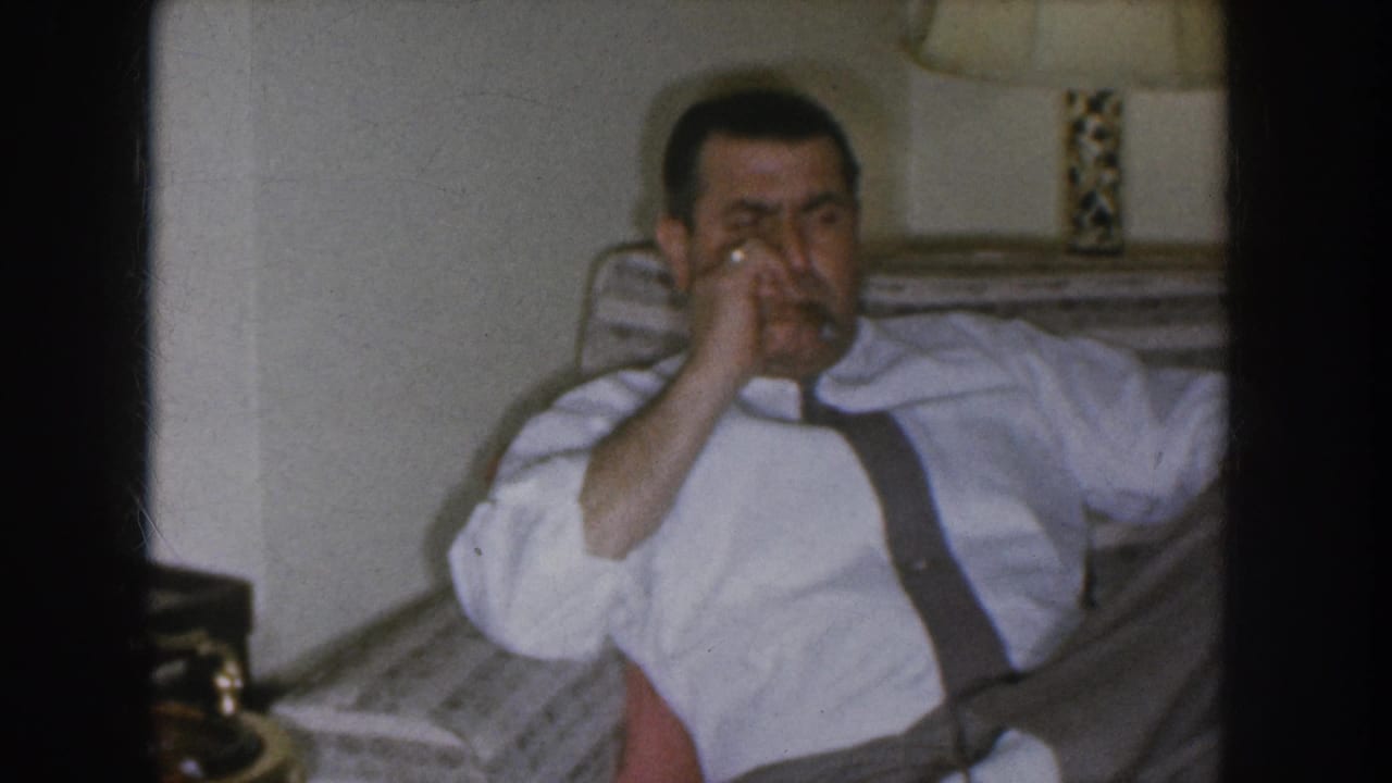 A man in a white dress shirt and dark suspenders brings a cigarette to his face in what appears to be a 1955 Nebraska living room.