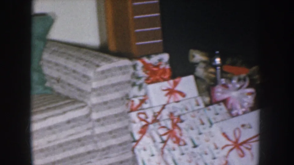 Wrapped Christmas gift stack with striped paper and red ribbon bows filmed on 8mm, Nebraska home movie circa 1955.