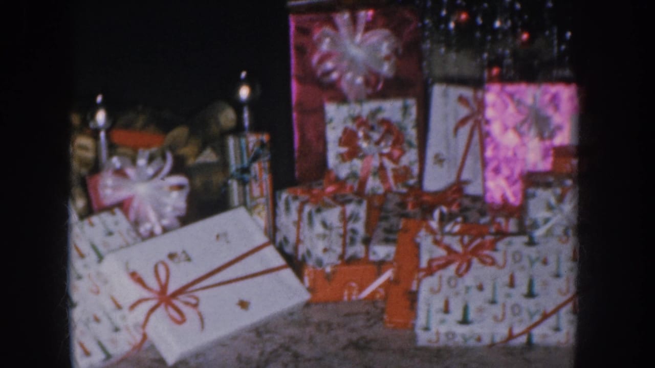 Christmas gift stack showing "Joy"-printed wrapping, red satin bows, and lit taper candles in background.