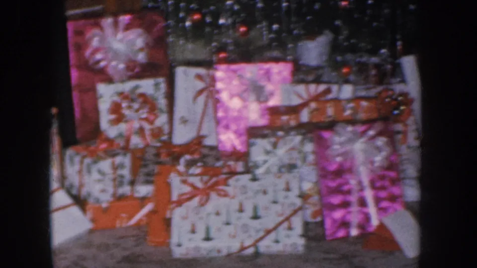Christmas gifts under tree base with round ornaments; pink foil and patterned wrapping with red bows; Nebraska home movie circa 1955.
