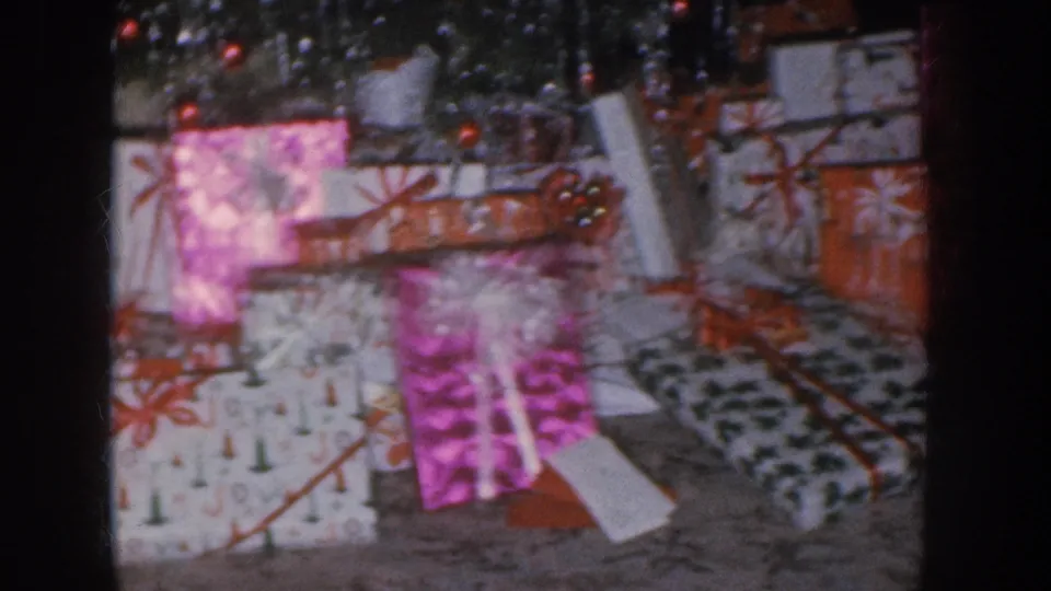 Wrapped Christmas gifts in mixed papers including pink and dark-pattern wrap with red bows; ornaments at top; Nebraska home movie circa 1955.