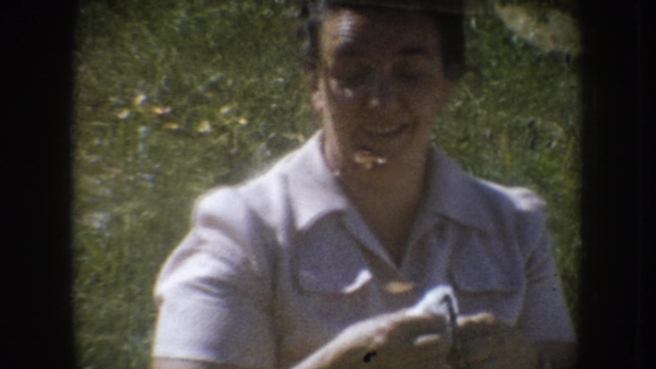 Woman in white collared shirt smiling while holding a small object in her right hand, green grass in background.