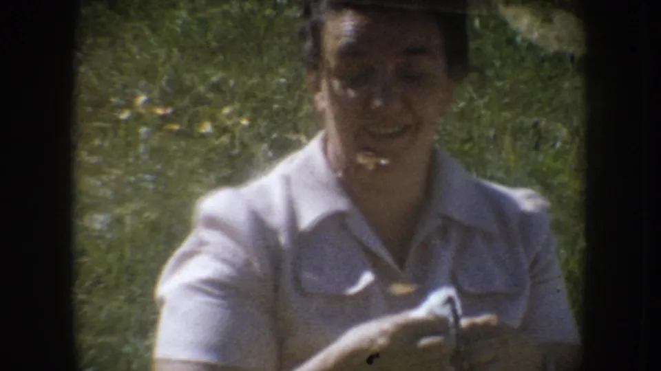 Mid-1950s woman in white collared shirt smiling while holding what may be eyeglasses or a cleaning cloth, outdoors on grass, South Dakota.