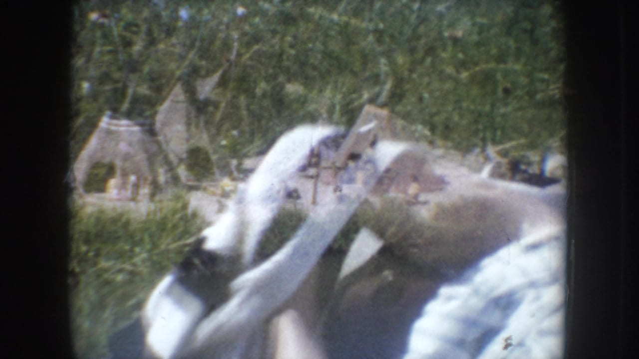 Close-up of a young girl in a light dress leaning toward a tipi-style diorama display, likely South Dakota, c.1955, 8mm home movie.