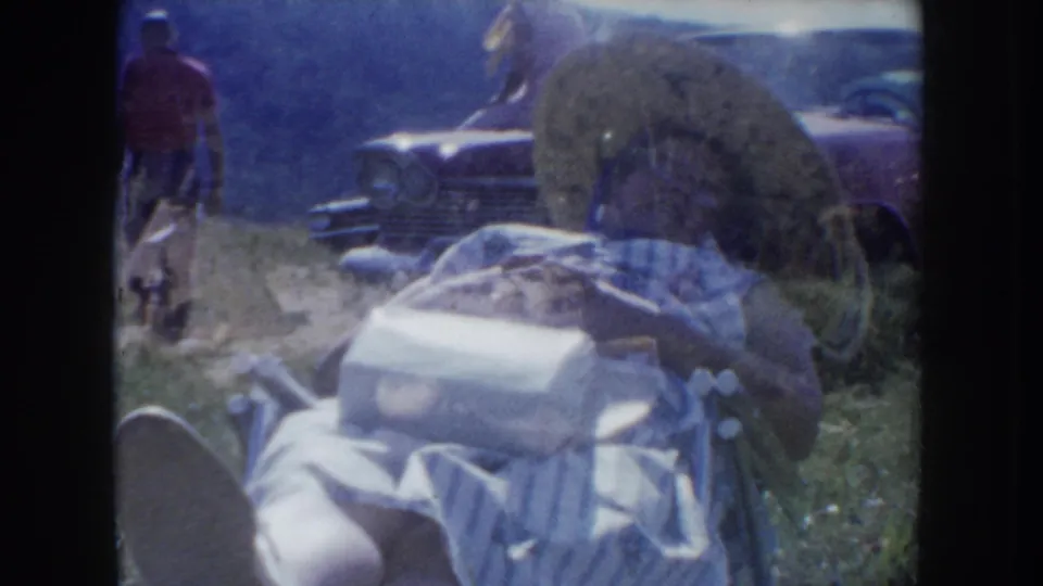 Outdoor diorama site with circular display element, a large-bodied 1950s automobile, and a figure in red clothing, South Dakota c.1955, 8mm home movie.