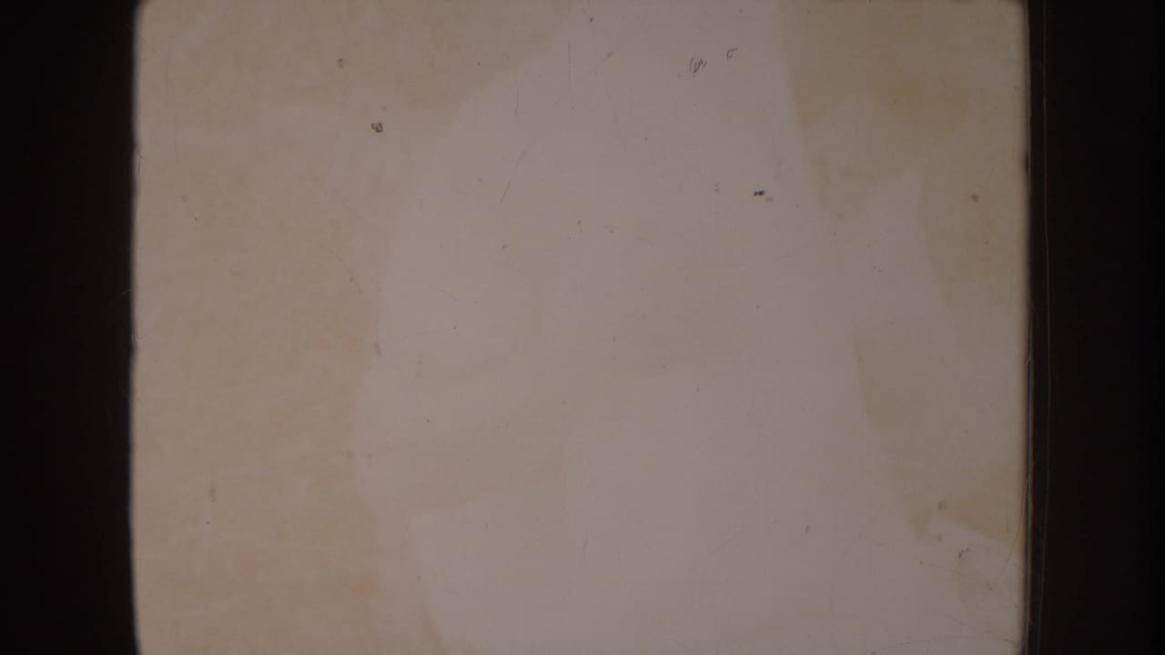 Heavily overexposed 8mm film frame, near-blank pale cream with faint discoloration and scattered film speckles.