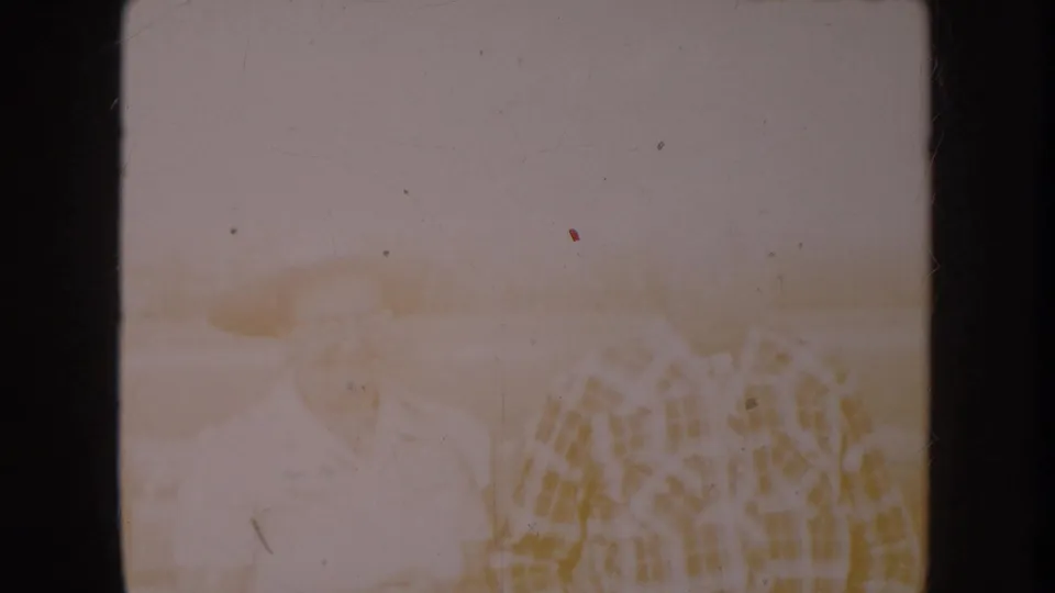 Near-blank overexposed frame from a circa 1955 8mm home movie; faint warm golden tones and a suggestion of patterned cloth or foliage appear in the lower-right corner.