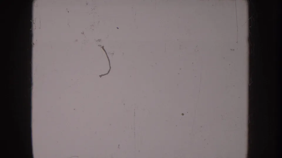 Overexposed or blank section of aged 8mm film showing only surface scratches, dust marks, and film grain — no subject matter legible.