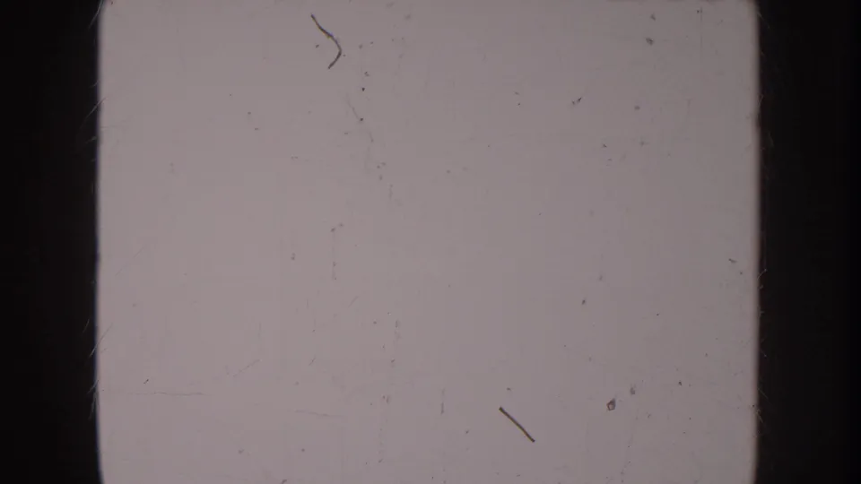 Second overexposed or blank section of aged 8mm film with diagonal scratch lines and dust particles visible on the emulsion surface.